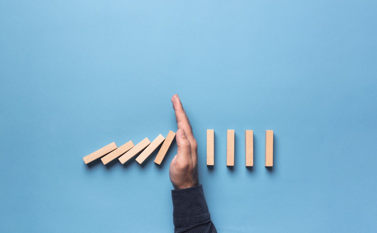 Hand stopping falling dominoes to illustrate the theme of business insolvency.
