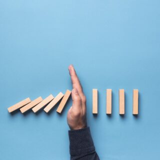 Hand stopping falling dominoes to illustrate the theme of business insolvency.