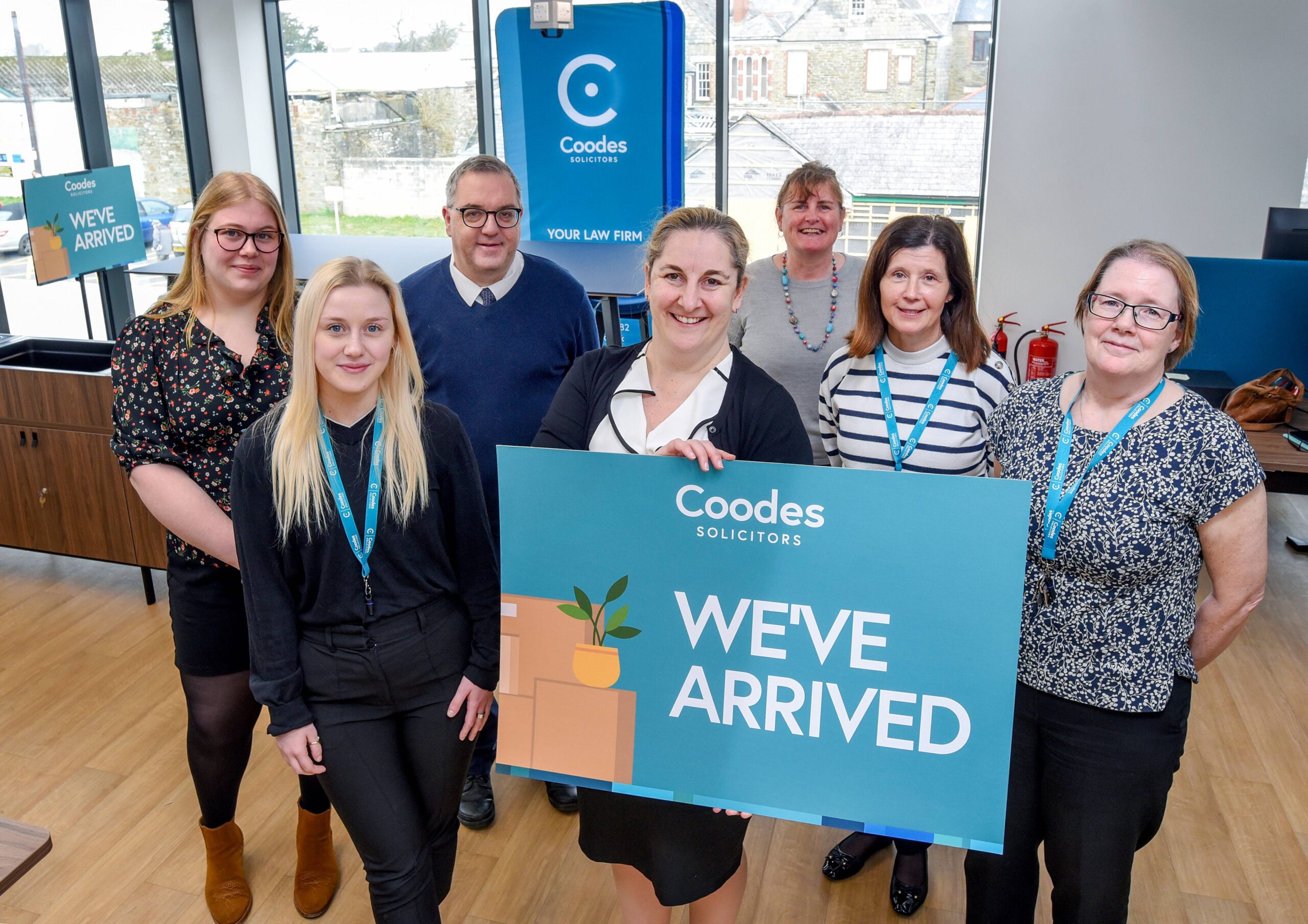 Members of the Coodes team are seen inside their new Liskeard office holding a large sign that says 'we've arrived'