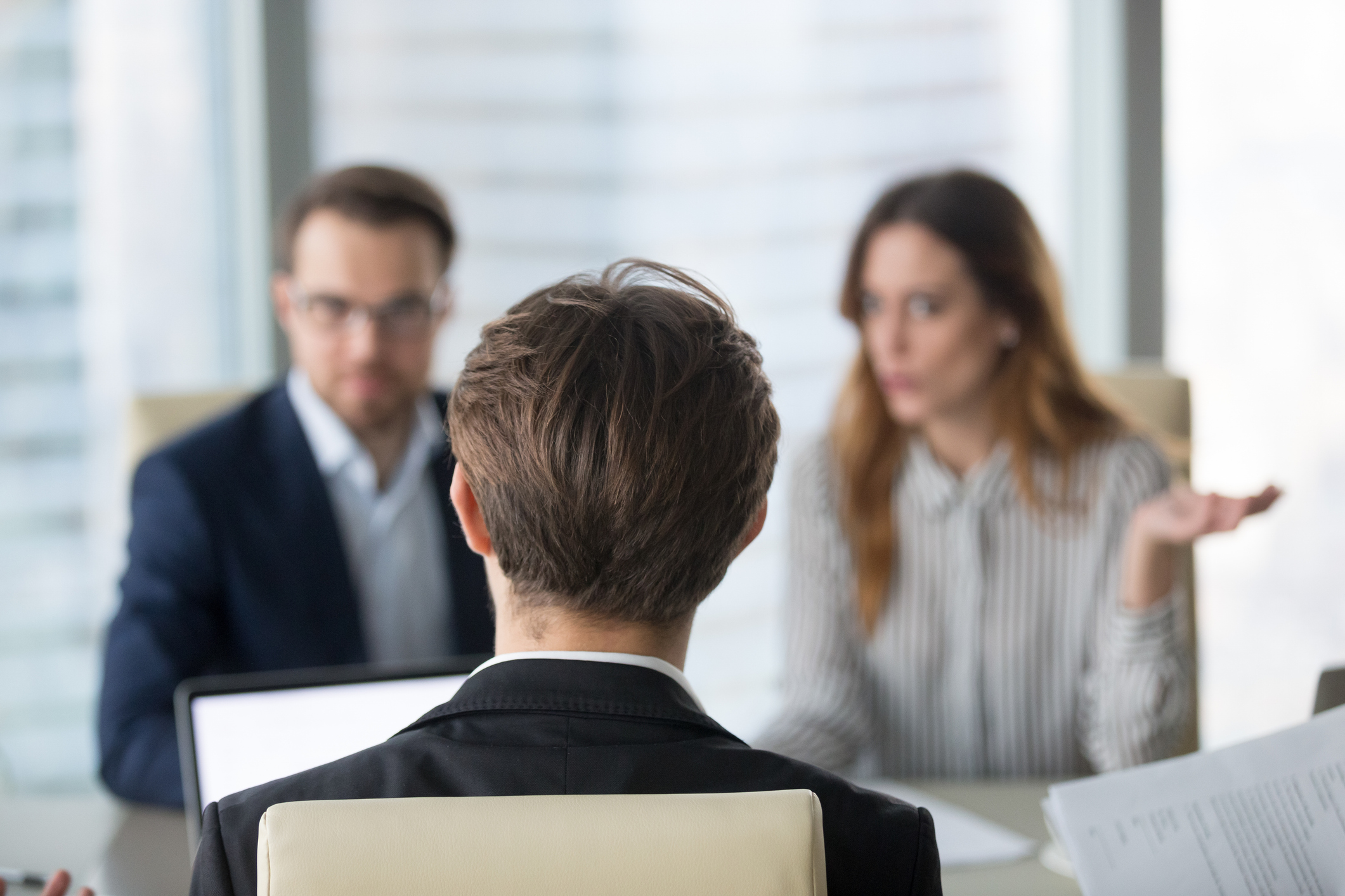Back view of a man sat infront of two other colleagues having a disciplinary meeting