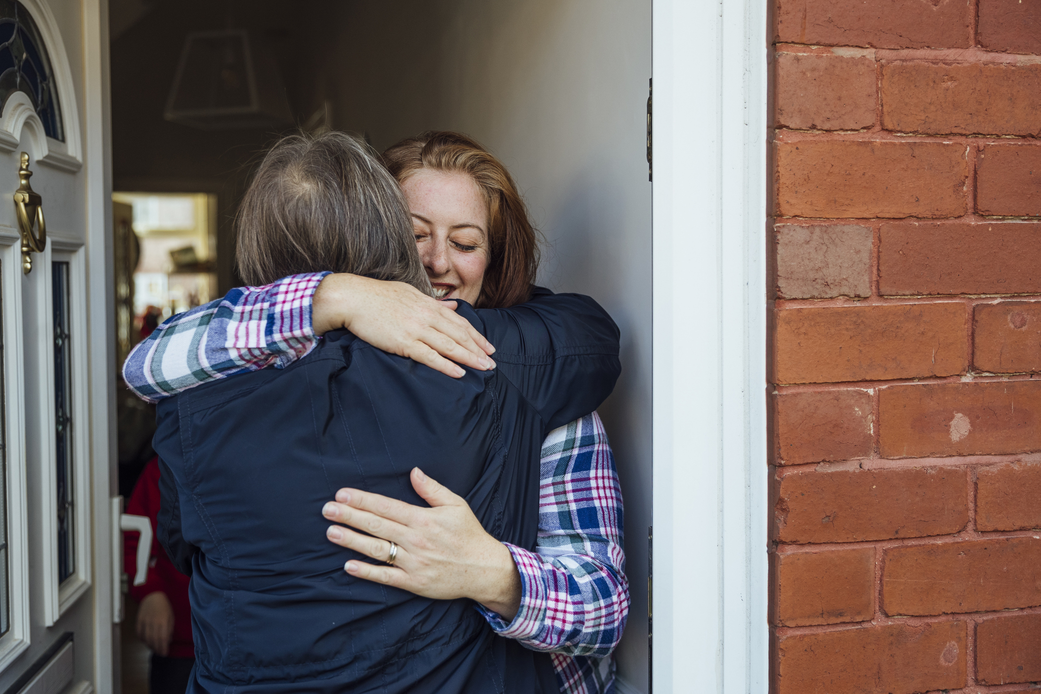 A mother and daughter exchange a hug in the doorway of the daughter's house.