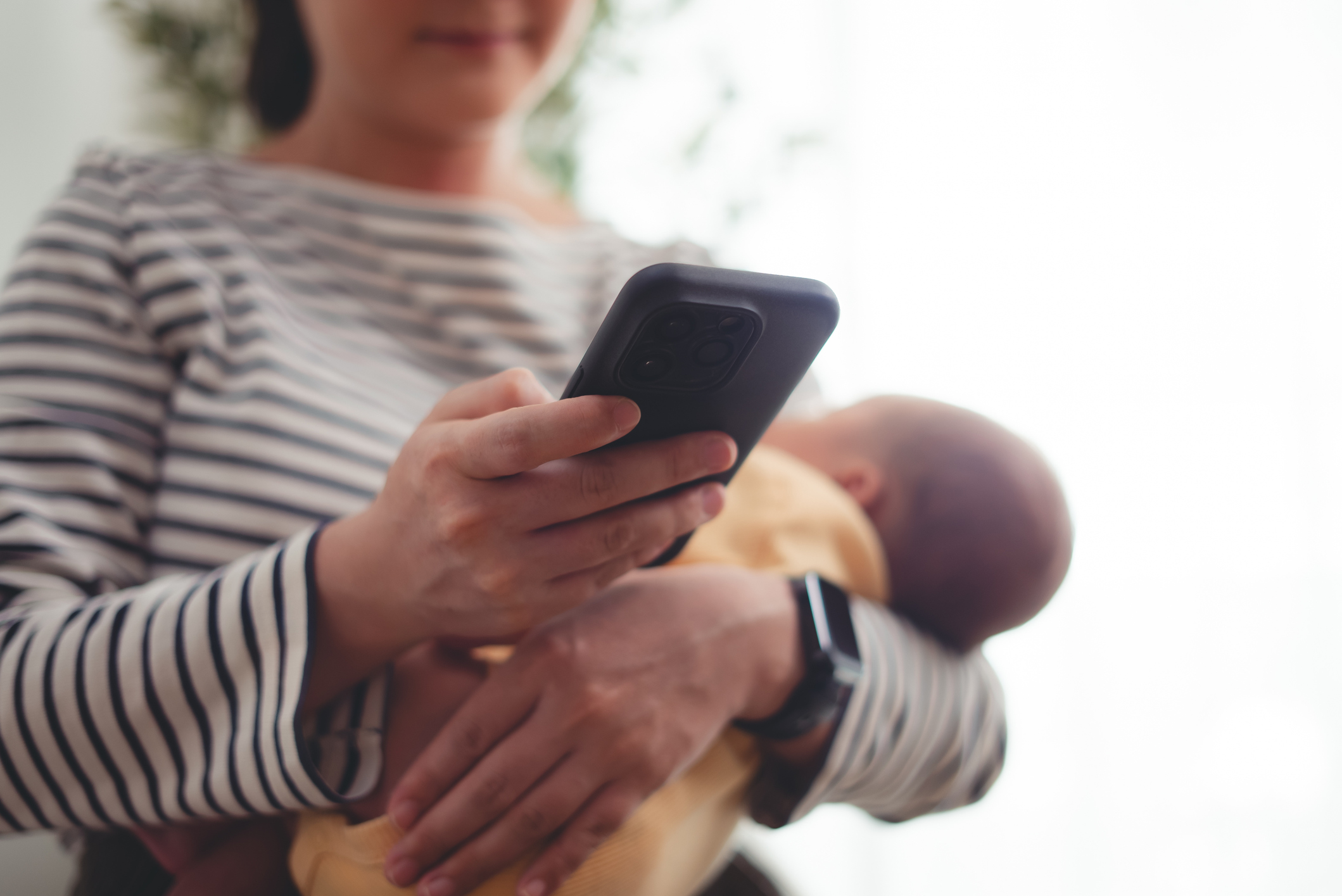 A low angle shot showing a woman holding her baby in one hand and her phone in the other.