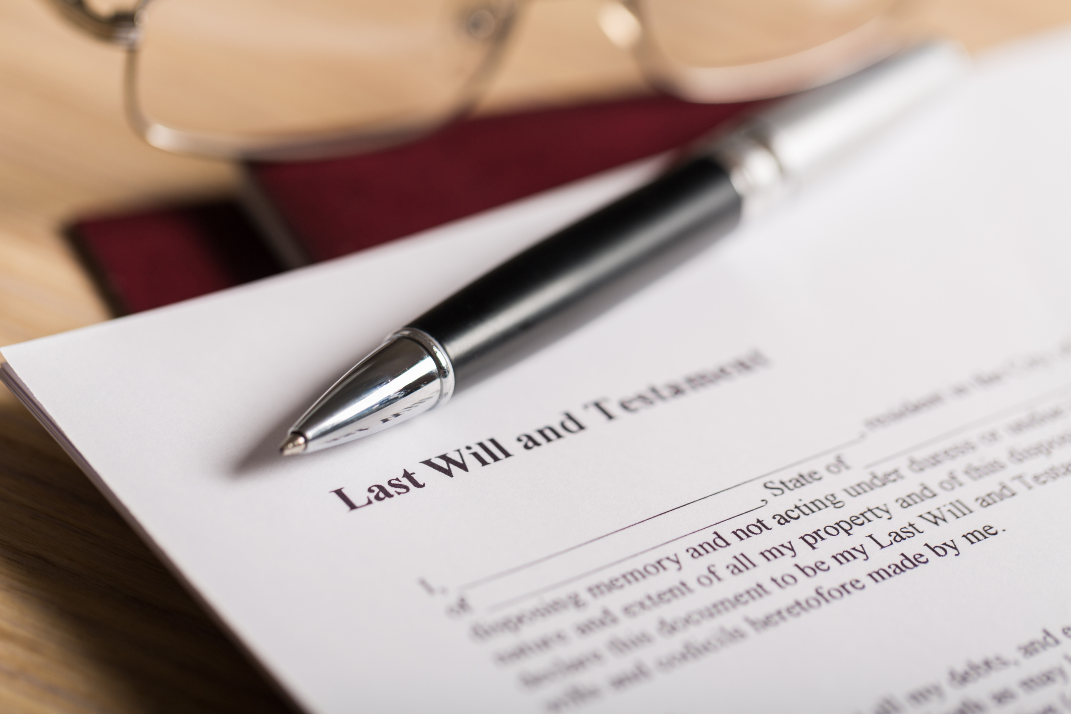 A pair of glasses are laid on a table and a pen laid on a piece of paper that says 'Last Will and testament'