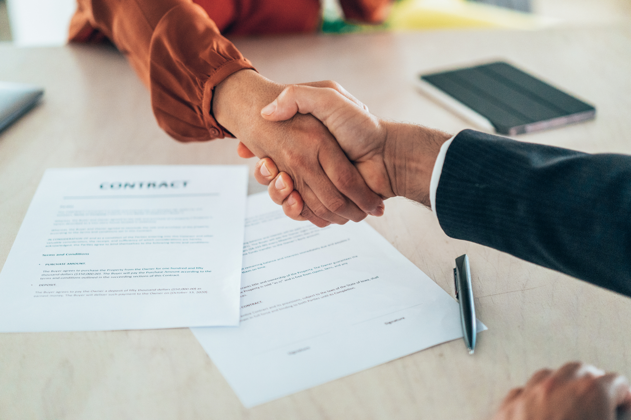 An employer and an employee shake hands over an employment contract on the table.