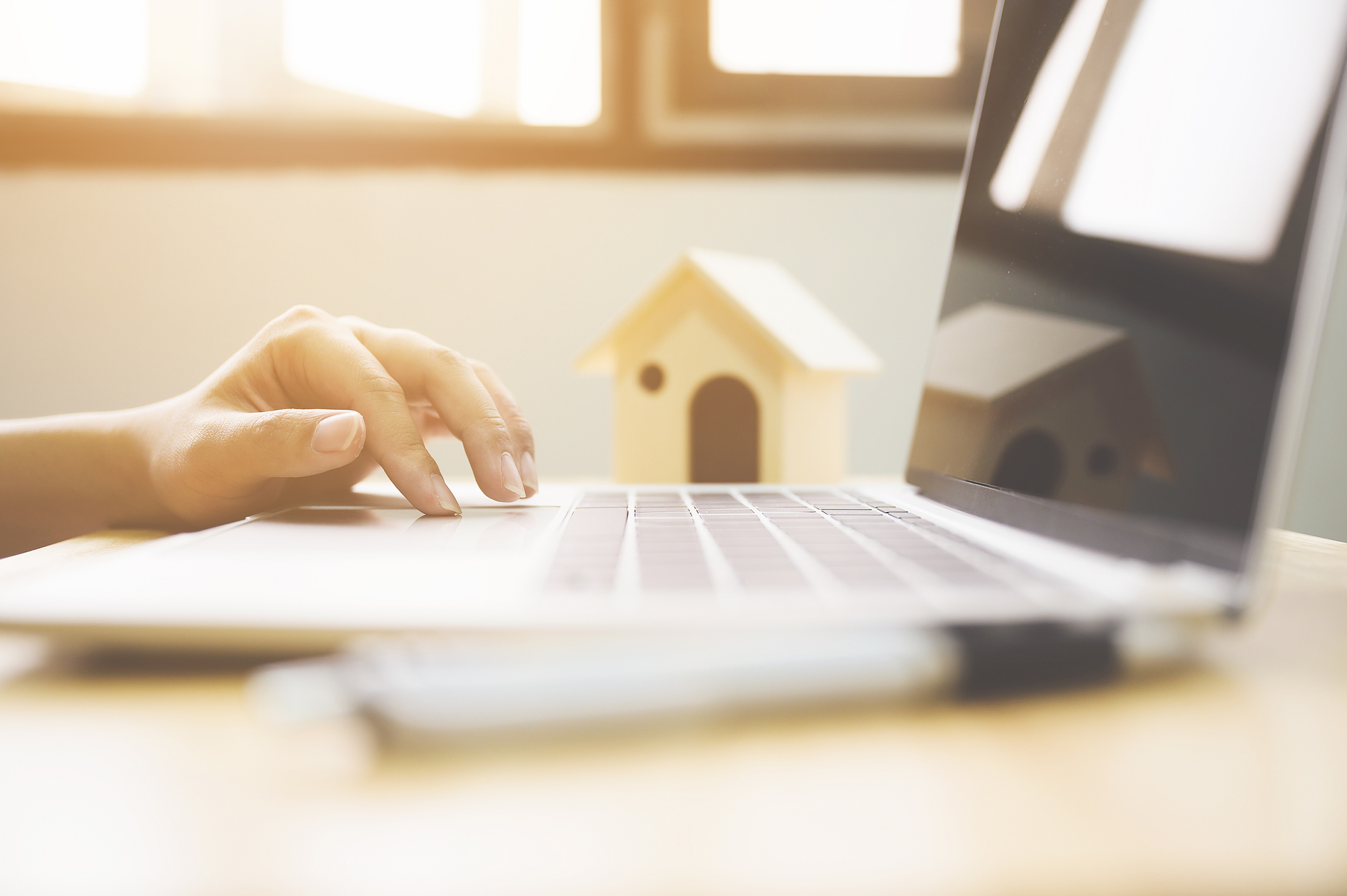 A hand uses a laptop, there is a miniature model house in the background.