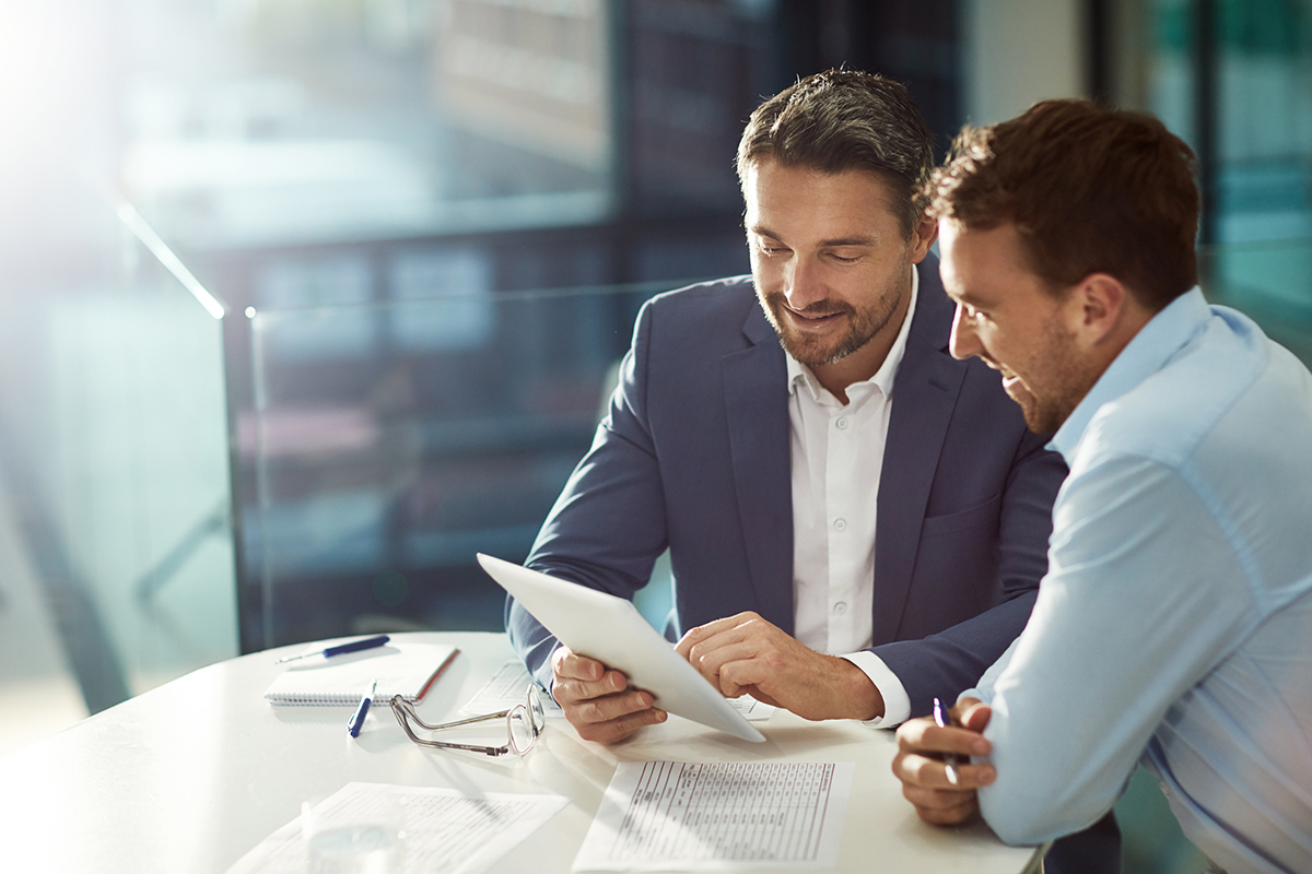 Two business men looking at a tablet and discussing a joint venture